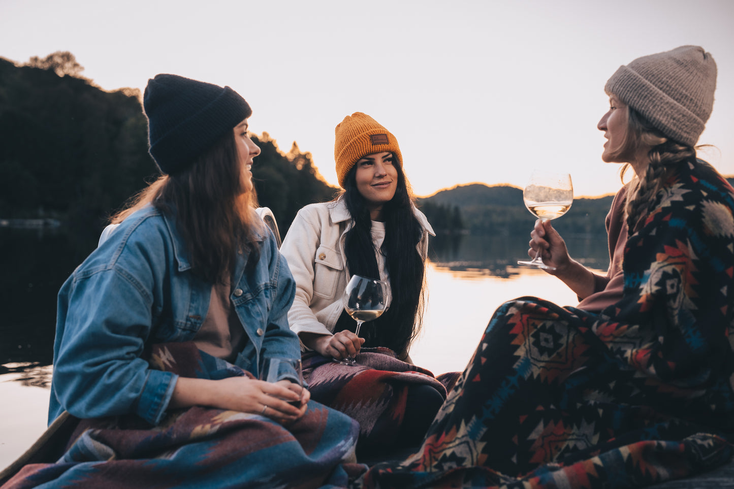 trois jeunes femmes au bord de l'eau bien emmitouflées avec couvertures boho et tuques