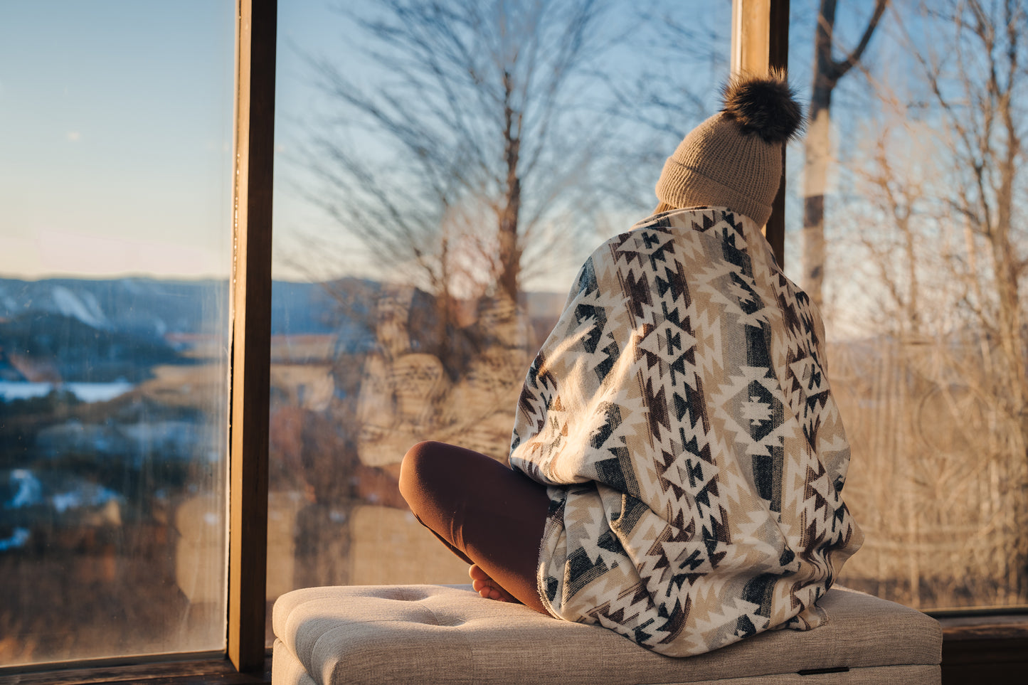Femme regardant un couché de soleil sur Mont-Tremblant dans un chalet enveloppée dans une couverture