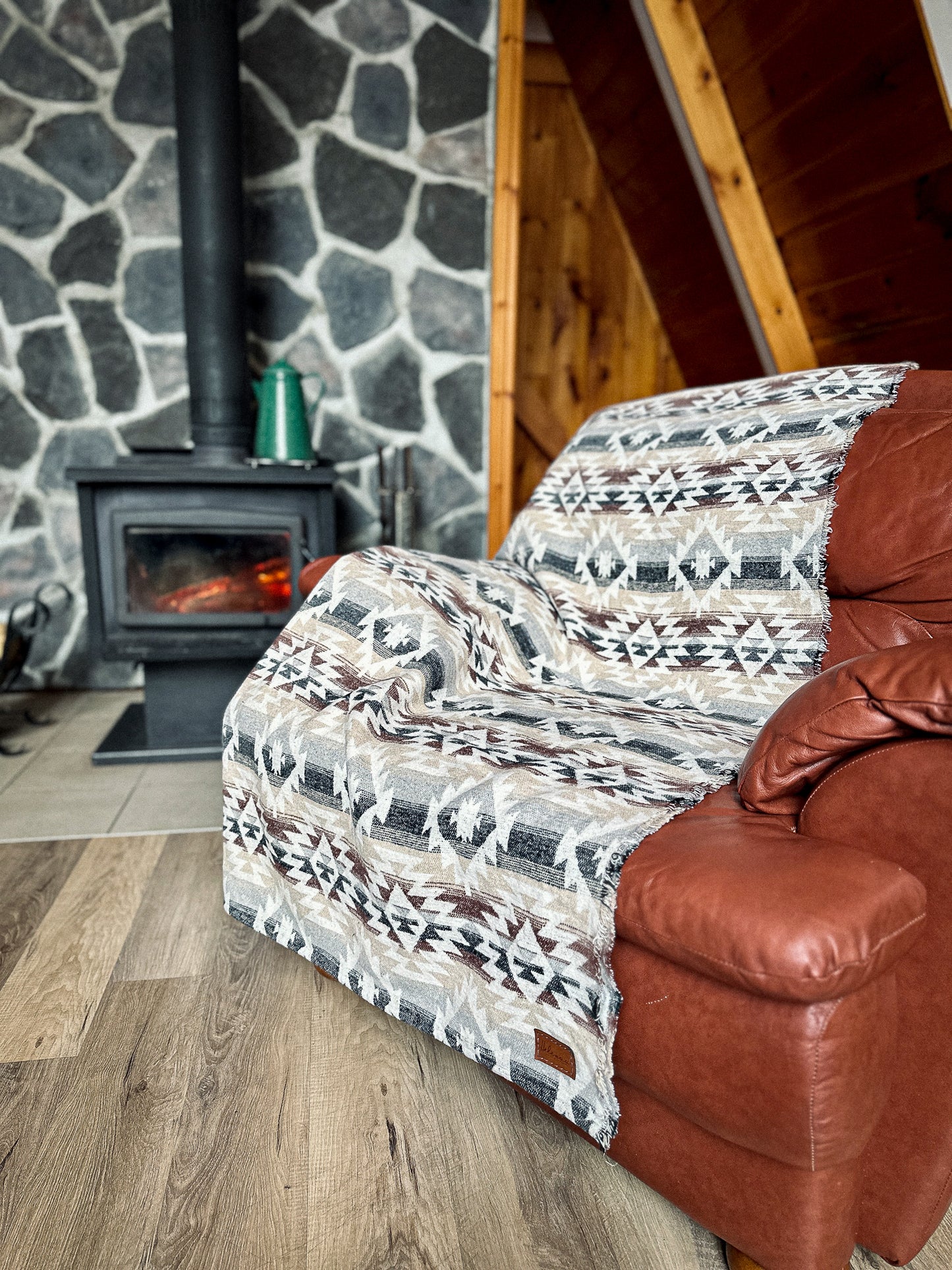 Couverture de laine boho sur un divan en cuir devant un feu de foyer au chalet